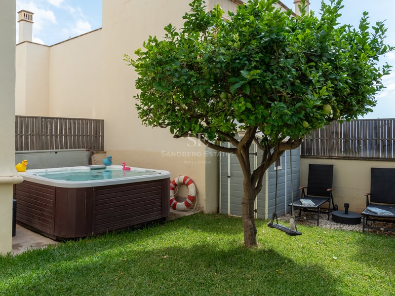 Petit jardin privé avec pelouse, jacuzzi en bois, un citronnier central et deux chaises longues noires.