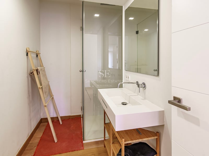 Modernt badrum med vitt tvättställ på träställning, duschvägg i glas och ljust trägolv.