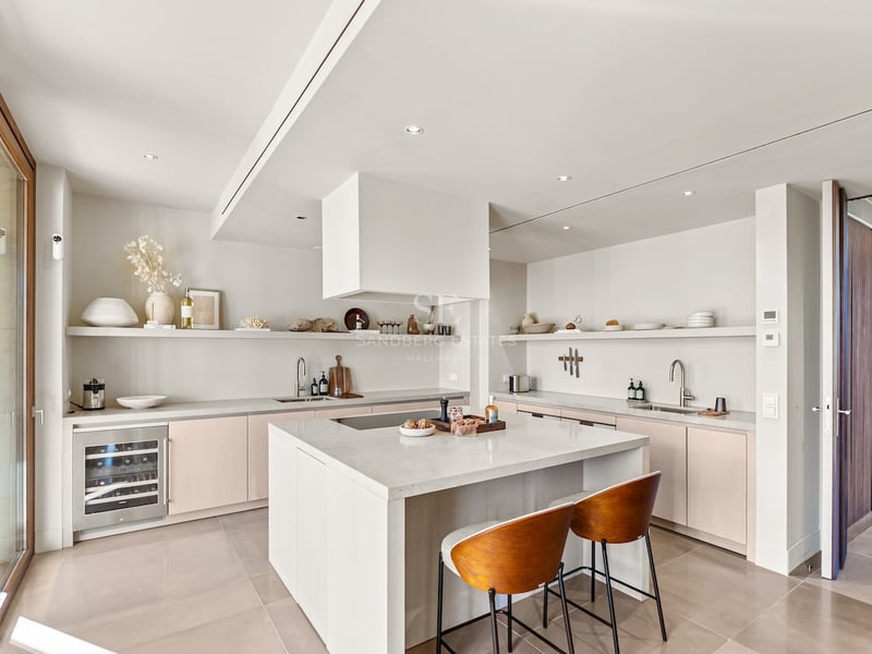 Cuisine moderne lumineuse avec îlot blanc, plans de travail en pierre, cave à vin et taburets en bois.