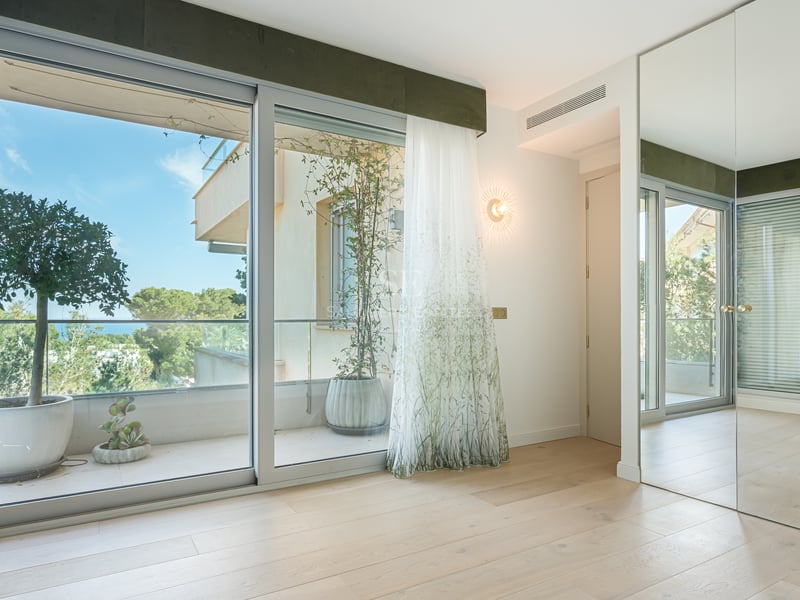 Bright bedroom with oak floors, mirrored wardrobes, and sliding glass doors opening to a terrace with garden views.