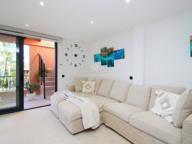 Ljust vardagsrum med en stor beige modulsoffa och skjutdörrar i glas som leder till en medelhavsterrass.