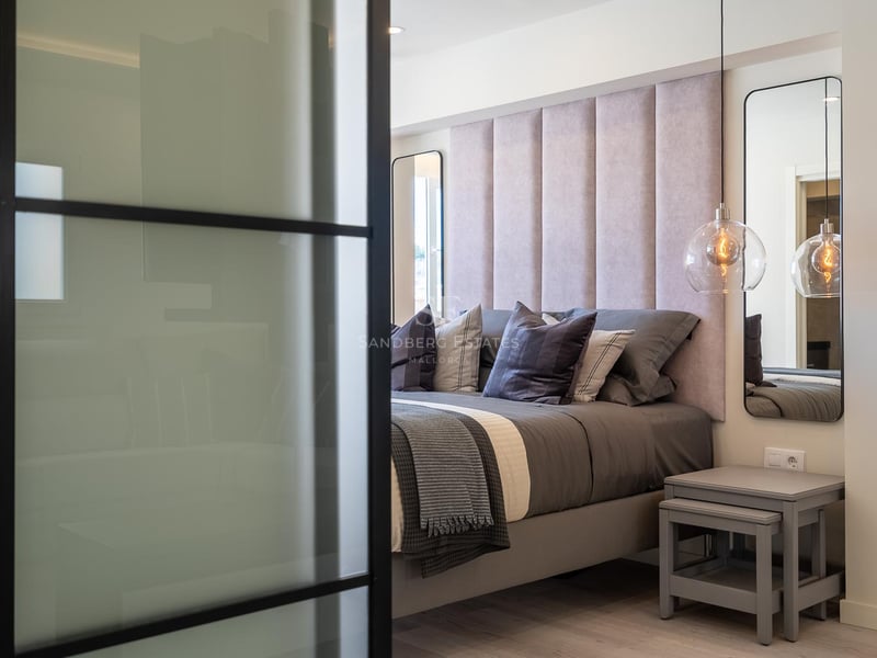 Detailansicht eines Hauptschlafzimmers mit rosa gepolstertem Kopfteil, Glaspendelleuchten und schwarzer Glastrennwand.