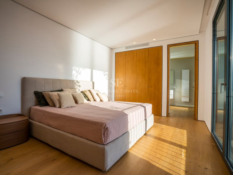 Modernes Schlafzimmer mit Eichenparkett, Einbauschränken, großem Bett und bodentiefen Glasfronten.