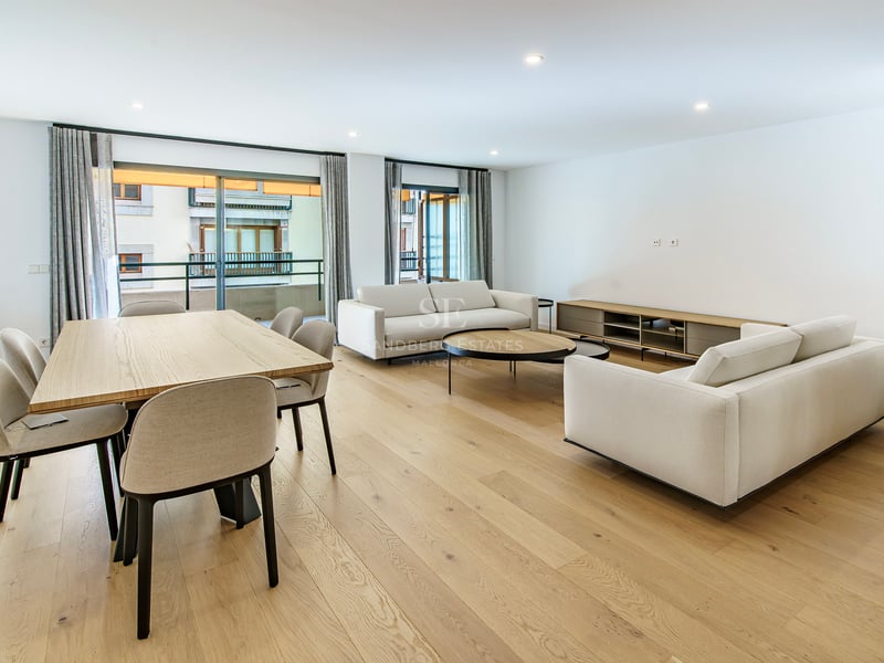 Séjour ouvert avec canapés blancs, table à manger en bois et grandes baies vitrées donnant sur un balcon.