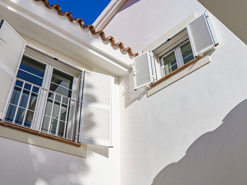 Detaljbild av vit fasad med mallorkinska fönsterluckor, terrakottatakpannor och fönsterbrädor i natursten.