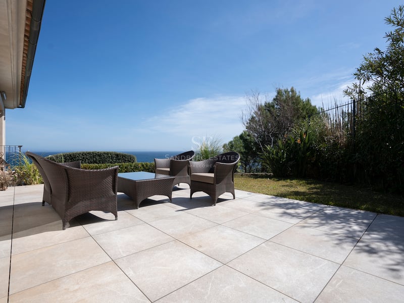 Große Steinterrasse mit dunklen Korbmöbeln und Blick auf das Meer unter klarem blauem Himmel.