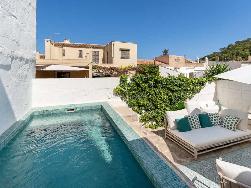 Piscine privée turquoise dans une cour avec murs blanchis à la chaux, sol en pierre et salon de jardin.