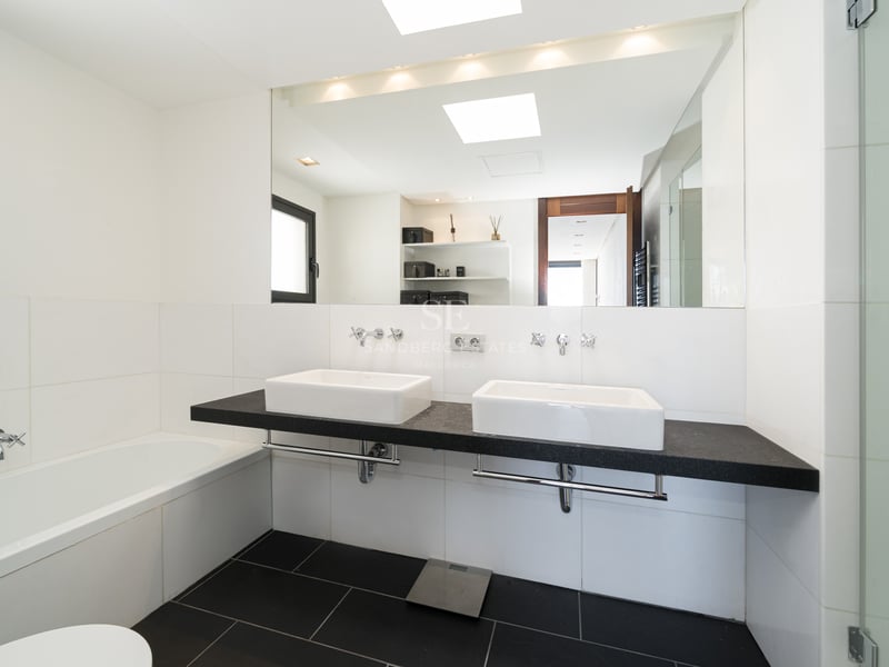 Bright modern bathroom featuring a black floating double vanity, white ceramic sinks, large mirror, and glass shower.