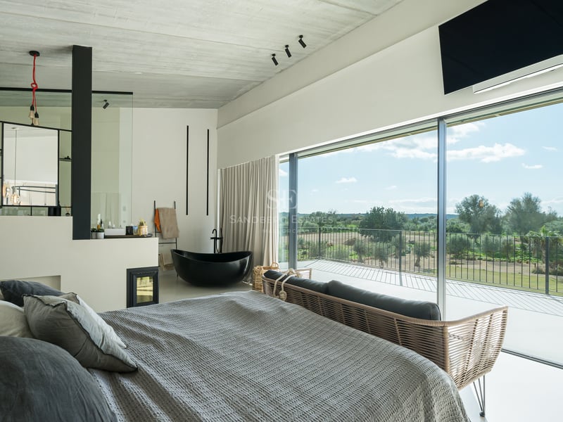 Modernt huvudsovrum med svart badkar, öppen spis och stora glaspartier mot det mallorkinska landskapet.