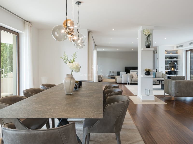 Grande table à manger en pierre avec chaises en cuir dans une pièce lumineuse avec parquet et baies vitrées.