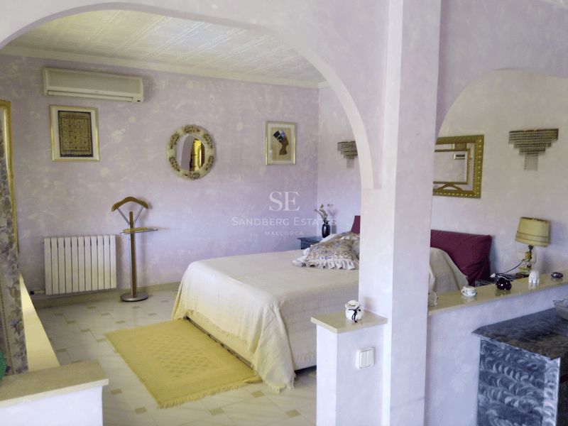 Dormitorio con paredes texturizadas color lila, arcos decorativos, cama doble y suelos cerámicos claros.