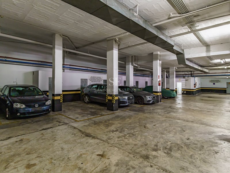 Grand garage souterrain avec piliers en béton, marquages de sécurité jaunes et voitures garées.