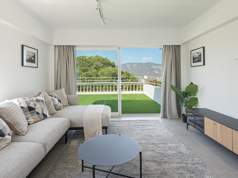 Salon moderne avec canapé d'angle gris et baies vitrées ouvrant sur une terrasse et un paysage de montagnes.