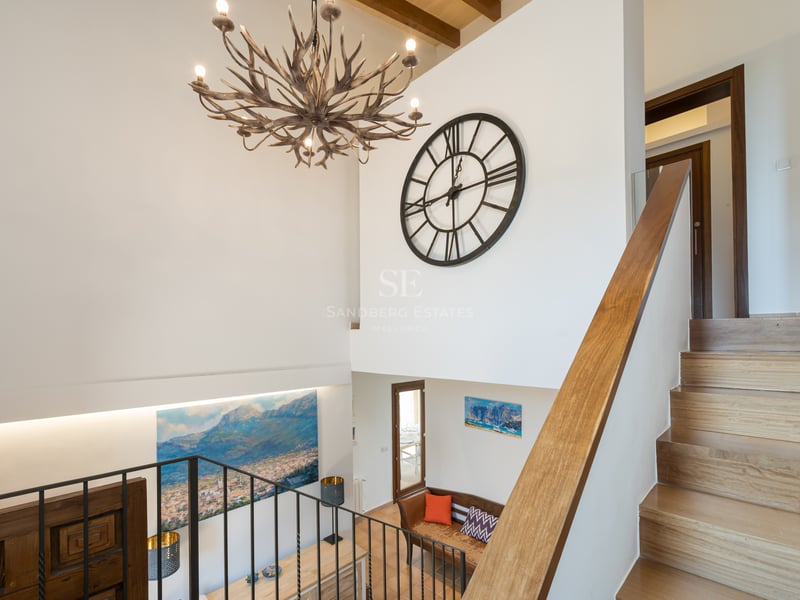 Vue intérieure d'un escalier en bois avec un grand lustre en bois de cerf et une horloge murale décorative.