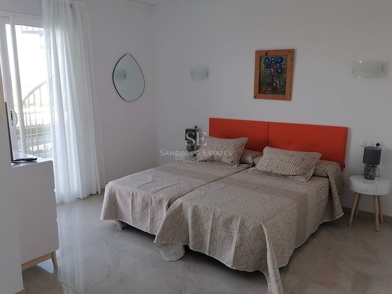 Chambre avec lits jumeaux, tête de lit orange, sol en pierre polie et accès direct au balcon.