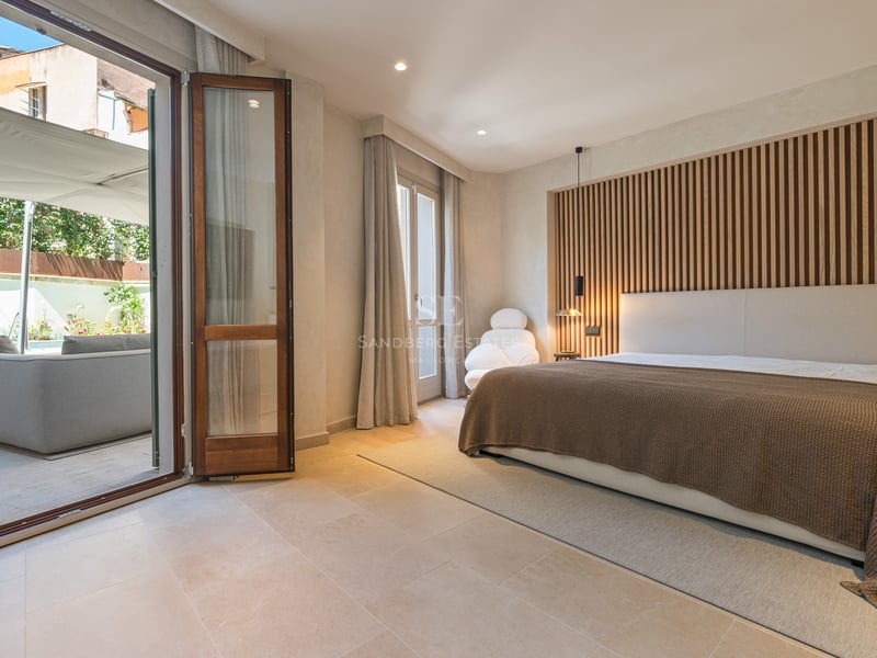 Chambre moderne avec mur en tasseaux de bois et grandes baies vitrées ouvrant sur un patio avec salon de jardin.