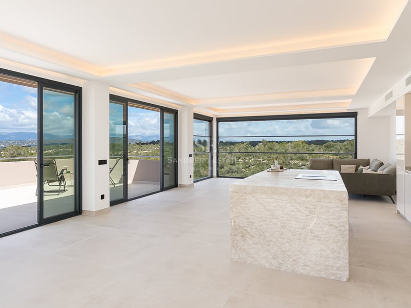 Heller Wohnraum mit monolithischer Steininsel, bodentiefen Glasfronten und Panoramablick auf die Berge.