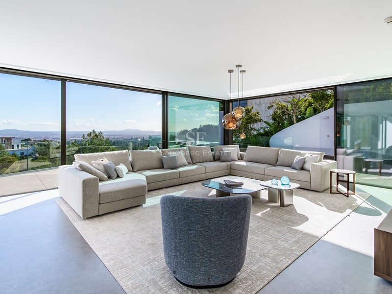 Salon moderne avec grand canapé gris et baies vitrées du sol au plafond donnant sur la vallée.