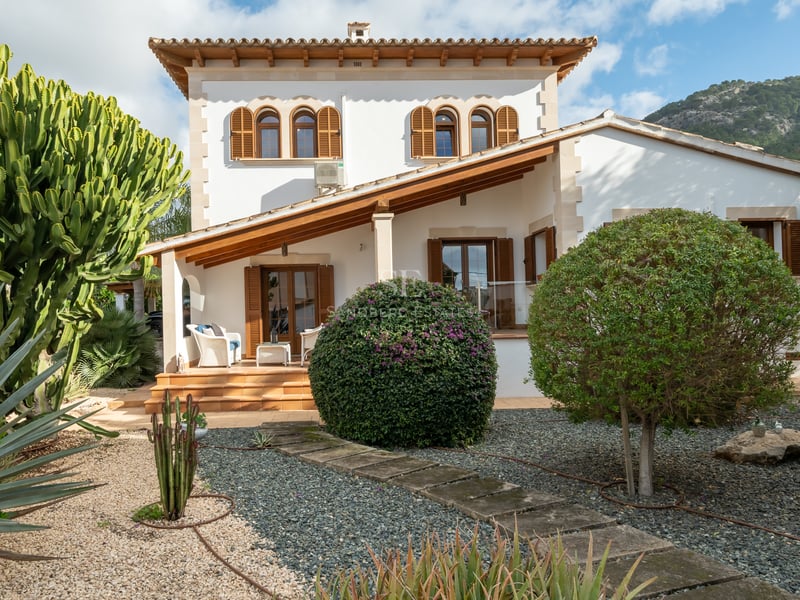 White villa facade featuring wooden shutters, terracotta roof, and a gravel garden with cacti and agave plants.