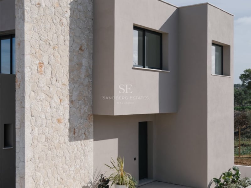 Außenansicht einer modernen Villa mit Natursteinwand, sandfarbenem Putz und anthrazitfarbenen Fensterrahmen.