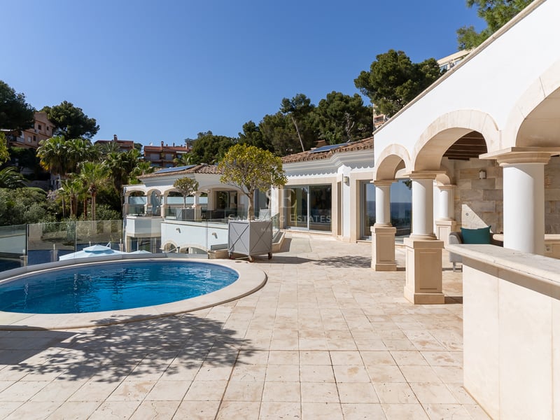 Luxusterrasse mit Natursteinboden, Bogensäulen und einem runden blauen Pool unter strahlendem Himmel.