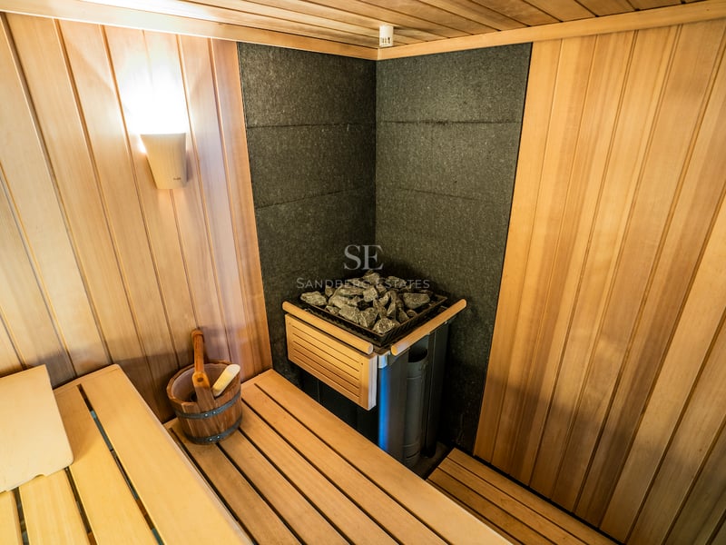 Innenansicht einer holzgetäfelten Sauna mit KLAFS-Steinofen, Holzeimer und stimmungsvoller Beleuchtung.