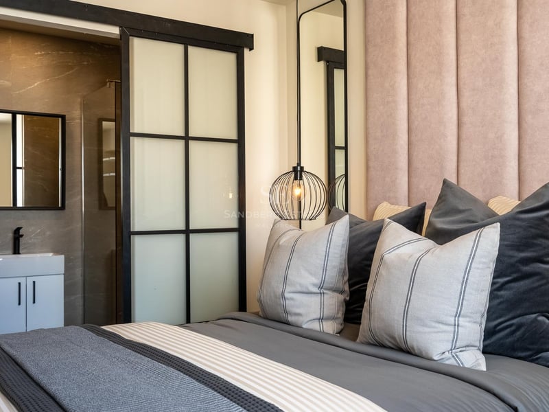 Schlafzimmer mit rosa Samtkopfteil, Designerlampe und industrieller Schiebetür zum Badezimmer.