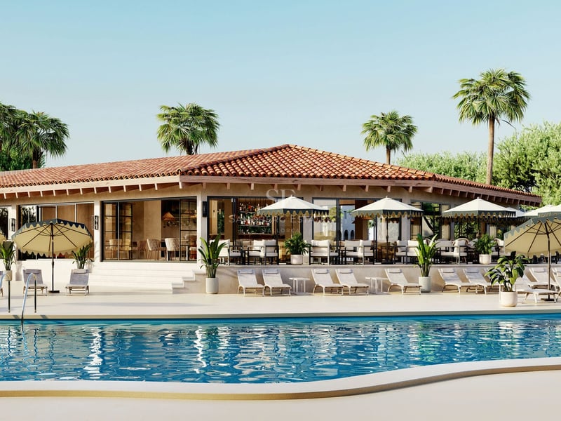 Grande piscine bleue devant un bâtiment avec toit en terre cuite, bains de soleil et parasols sous un ciel dégagé.