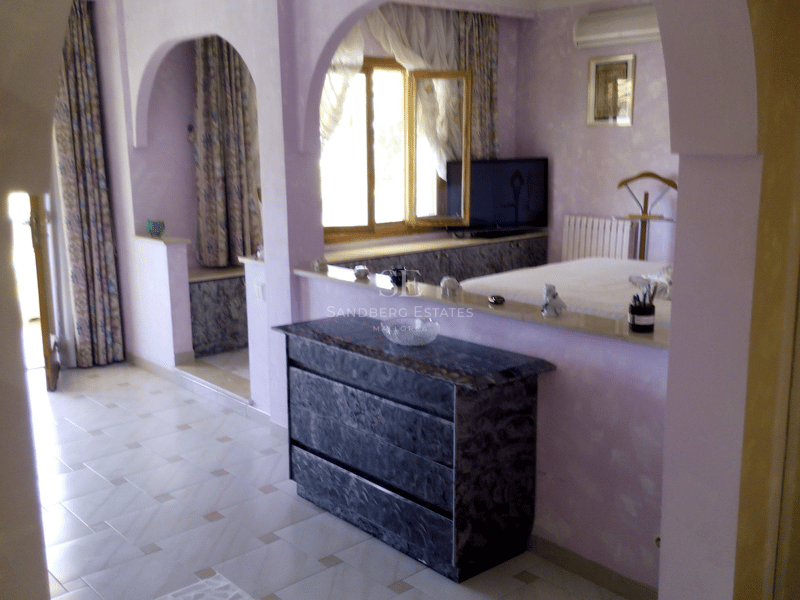 Dormitorio principal en tonos lavanda con arcos arquitectónicos, cómoda de mármol y suelos de baldosa clara.