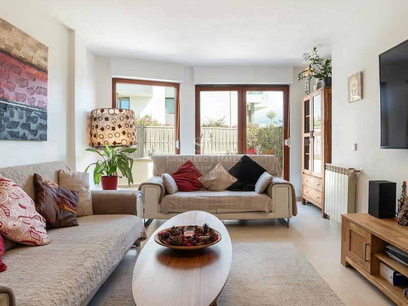 Un salon ensoleillé avec des canapés beiges, des meubles en bois et des baies vitrées ouvrant sur une terrasse.