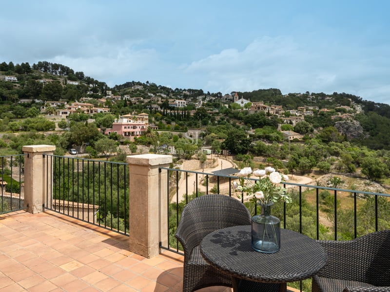 Terrasse en terre cuite avec mobilier en rotin et garde-corps en fer forgé surplombant un village méditerranéen.