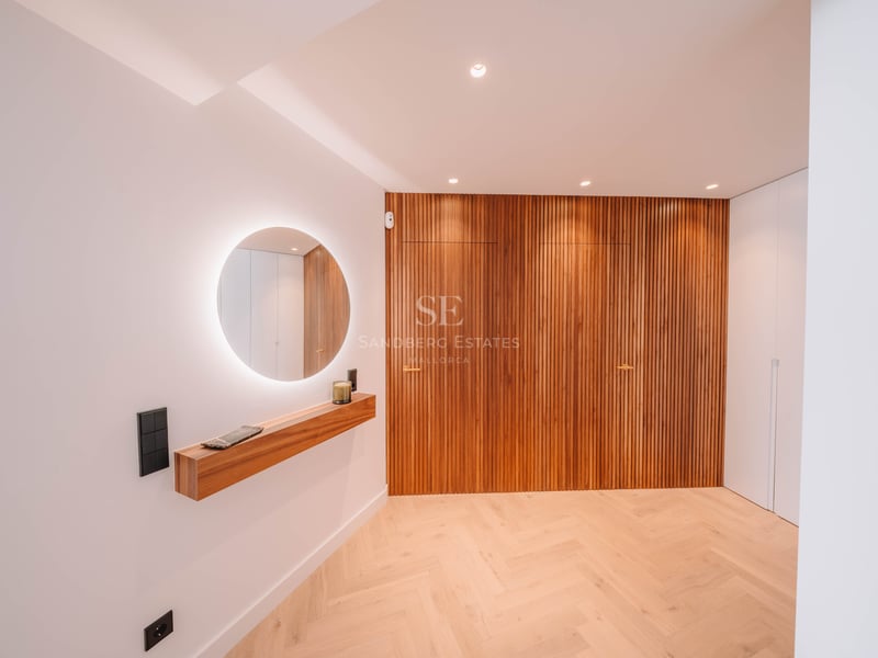 Couloir minimaliste avec miroir rétroéclairé, étagère en bois et mur en lattes verticales.