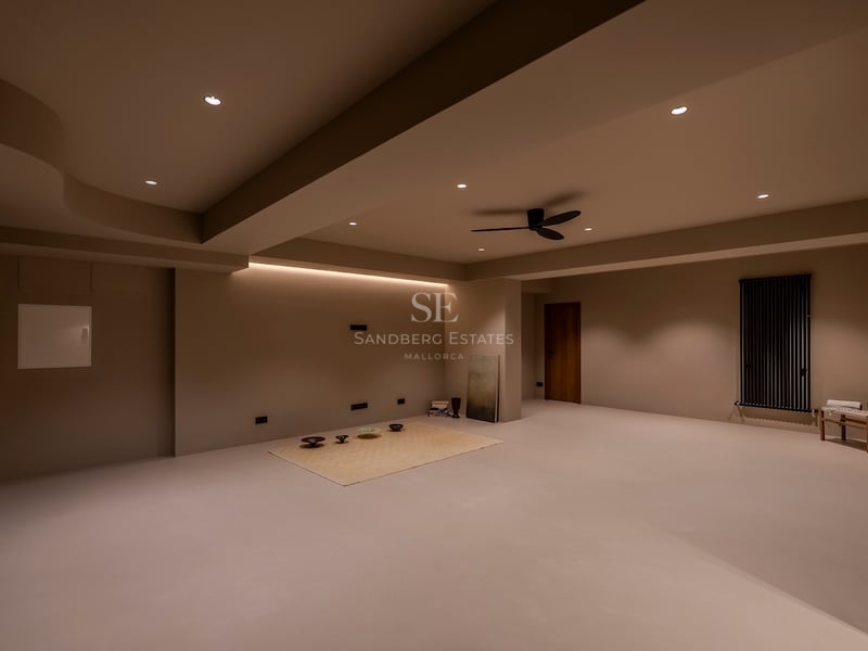 Une grande pièce minimaliste aux murs et sols beiges, avec éclairage encastré et ventilateur de plafond.