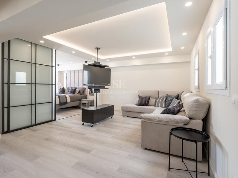 Zeitgenössisches Wohnzimmer mit grauem L-Sofa, drehbarer TV-Halterung und Glasschiebetüren zum Schlafzimmer.