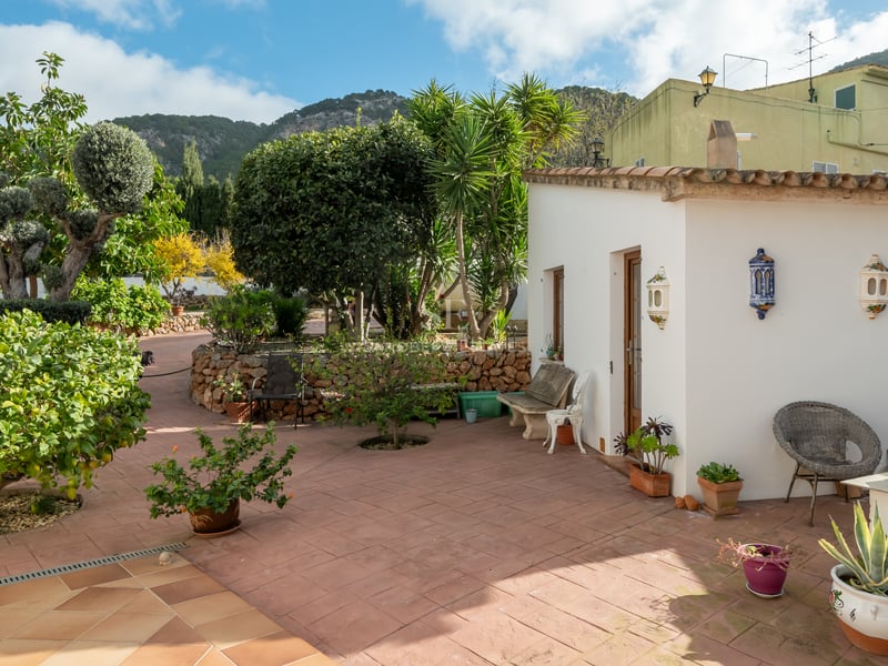 Sun-drenched terracotta patio featuring a whitewashed annex, lush Mediterranean gardens, and mountain views.