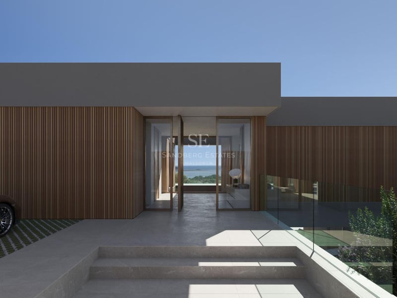 Entrée de villa minimaliste avec lattes de bois, portes pivotantes en verre et vue mer à travers le hall.
