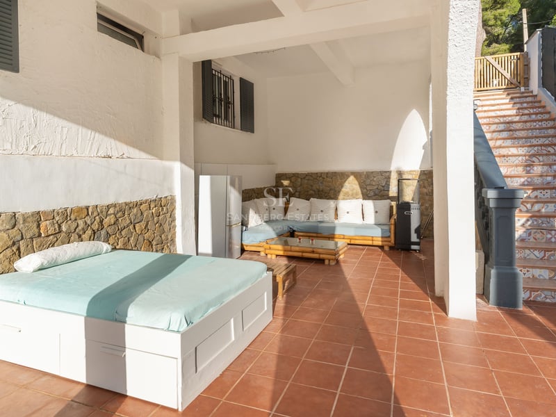Terrasse couverte avec sols en terre cuite, lit de jour extérieur, banquette, murs en pierre et escalier carrelé.