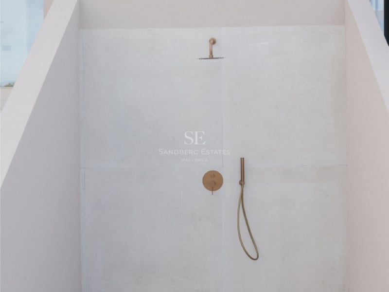 Minimalistische Außendusche mit gebürsteten Messingarmaturen vor hellbeige Steinwänden.