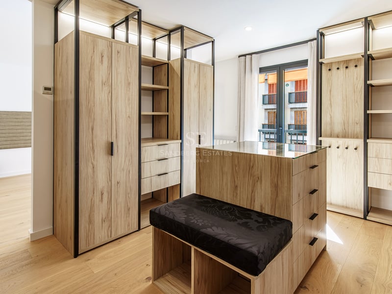 Grand dressing avec armoires en bois clair, îlot central avec plateau en verre et banc noir.