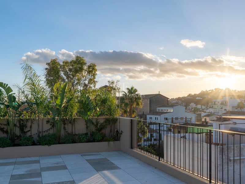 Terrasse de toit moderne avec carrelage en pierre et plantes tropicales, surplombant une ville méditerranéenne au coucher du soleil.