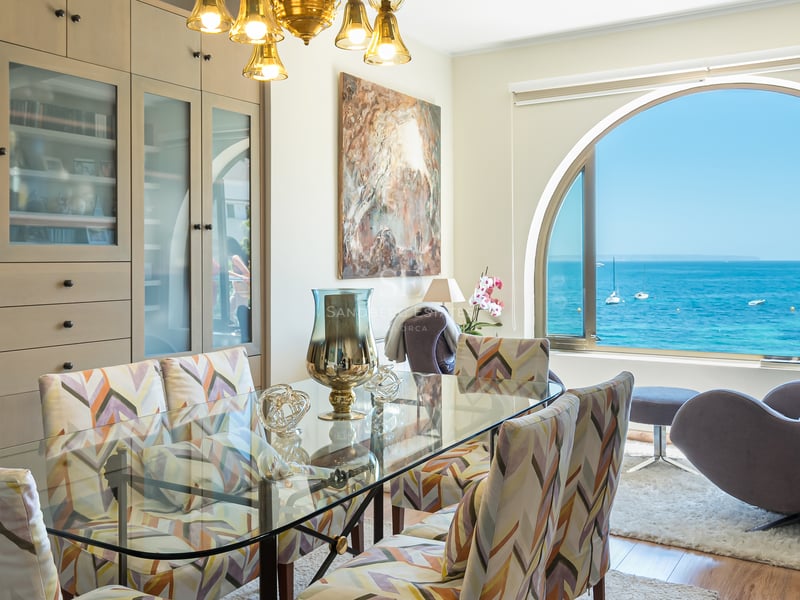Matsal med glasbord och ett stort välvt fönster med utsikt över det blå havet och båtar.