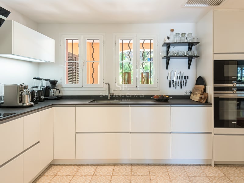 Modern white kitchen featuring dark countertops, integrated Siemens appliances, and traditional patterned tile flooring.