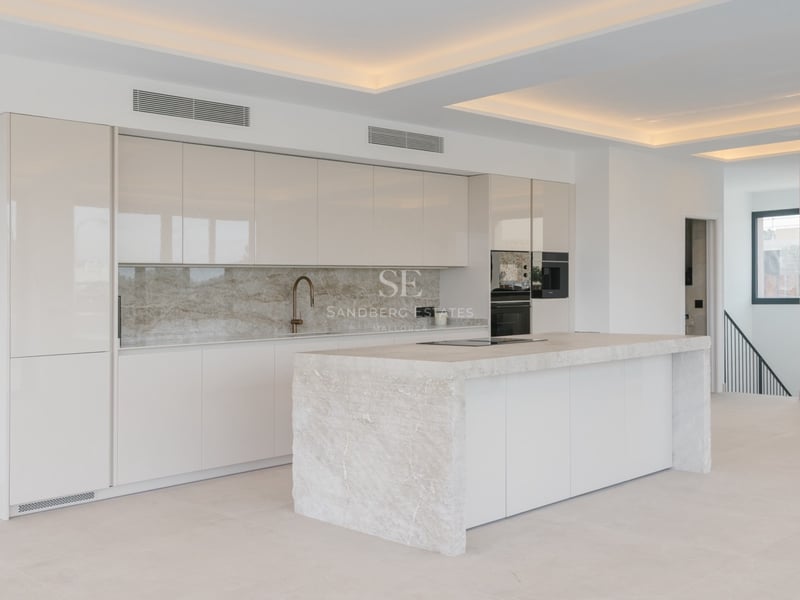 Moderne Luxusküche mit großer Natursteininsel, Hochglanzschränken und LED-Lichtvoute an der Decke.