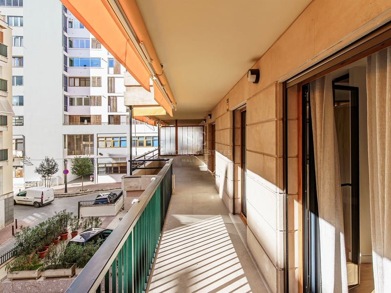 Long balcon ensoleillé avec auvent orange et balustrade métallique donnant sur une rue urbaine.