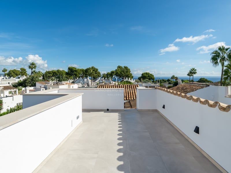 Vaste toit-terrasse blanc avec dalles en pierre claire, offrant une vue panoramique sur les palmiers et la mer.