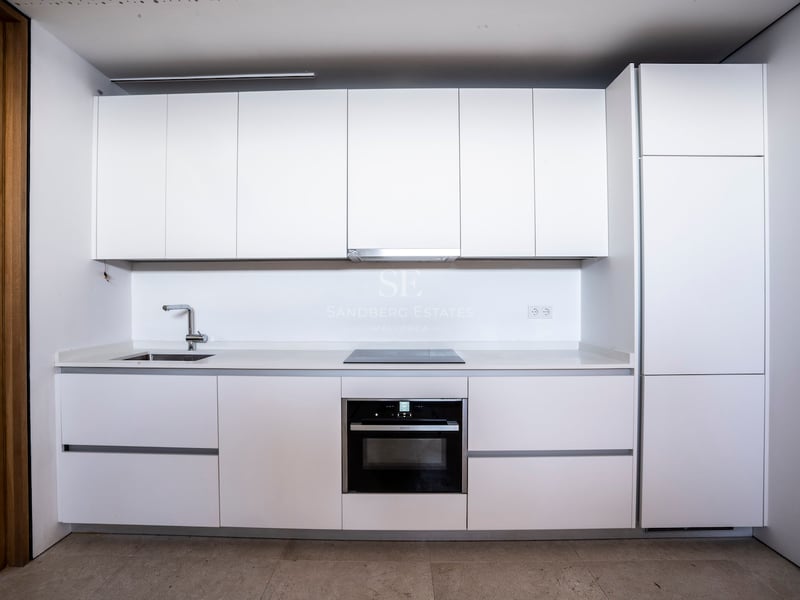 Weiße moderne Küche mit grifflosen Schränken, Einbaubackofen, Induktionskochfeld und Edelstahlspüle.