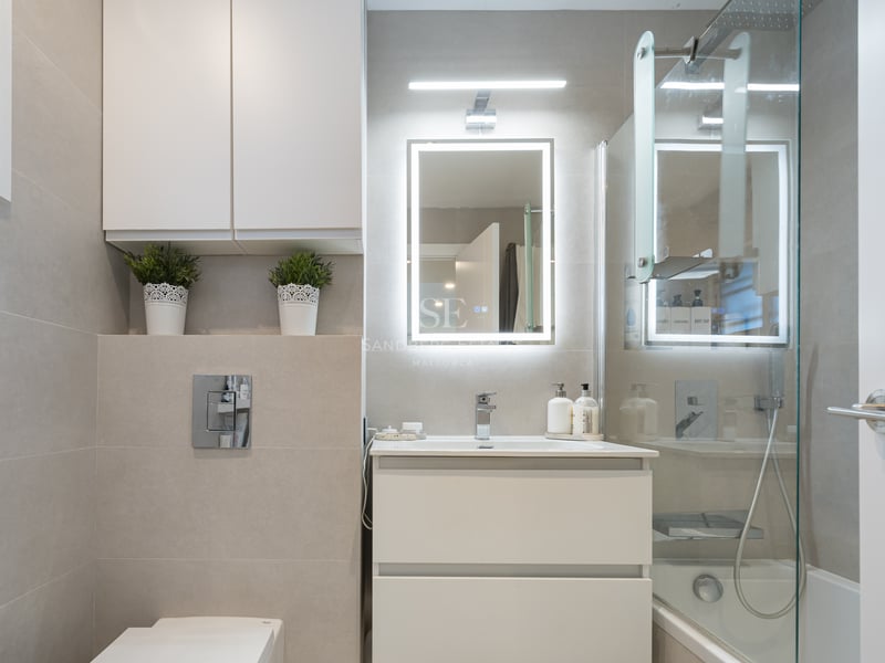 Modern bathroom with white vanity, backlit LED mirror, glass shower screen, and beige large-format tiles.