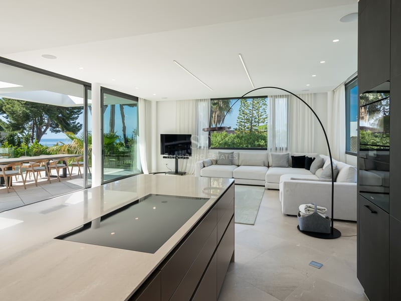 Salon contemporain et îlot de cuisine avec baies vitrées ouvrant sur une terrasse face à la Méditerranée.