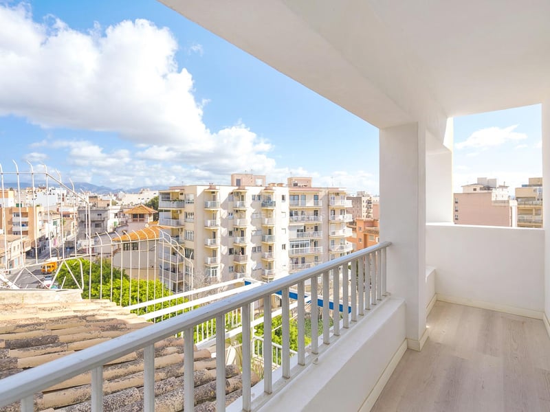 Heller weißer Balkon mit hellem Holzboden und Blick auf Stadtgebäude und Berge im Hintergrund.