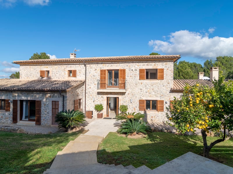 Tvåvåningsvilla i natursten med bruna fönsterluckor i trä, tegeltak och ett citronträd i förgrunden.